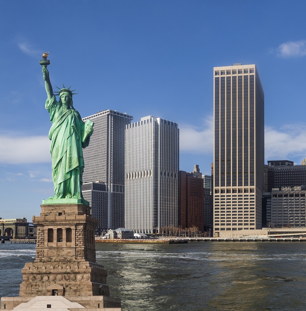 Kip svobode stoji ob reki pred visokimi poslovnimi stolpnicami na ozadju modrega neba v New Yorku